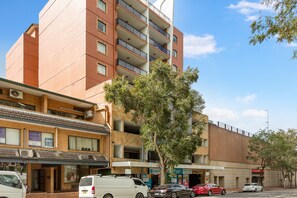 A multi-story building with a brick facade, a tree in front, and several parked cars. - Spacious 2-Bed Apartment Near Parramatta CBD (Parramatta)
