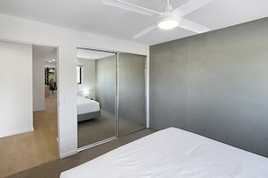 A modern bedroom with a bed, a ceiling fan, and a sliding door leading to a bathroom. - Coastal Pool 3-Bed Townhouse Near Broulee Beach (Broulee)