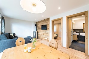 A modern living room with a wooden dining table, sofa, and a TV mounted on a wooden wall. - Apartment 'Hütterhof Aschbach "Holunder"' with Mountain View and Wi-Fi (Lagundo)