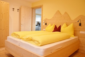 A bedroom with a wooden bed, a wooden door, and a kitchen visible through an open door. - Apartment 'Hütterhof Aschbach "Holunder"' with Mountain View and Wi-Fi (Lagundo)