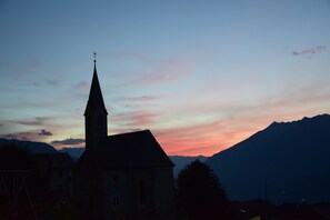 A church with a tall steeple against a sunset sky. - Apartment 'Hütterhof Aschbach "Holunder"' with Mountain View and Wi-Fi (Lagundo)