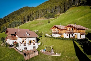 A chalet-style building with a wooden exterior and a white facade, situated on a grassy hillside with a forested backdrop. - Apartment 'Hütterhof Aschbach "Holunder"' with Mountain View and Wi-Fi (Lagundo)