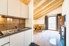 Eine moderne Küche mit weißen Schränken und einer Holz Arbeitsplatte, ein Essbereich mit einem Holztisch und Stühlen, sowie ein Balkon mit Aussicht.