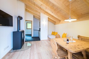 Cozinha moderna com fogão embutido, sala de jantar com mesa e cadeiras de madeira, e TV fixada na parede.