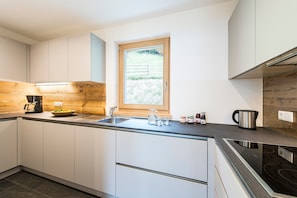 Eine moderne Küche mit weißen Schränken, einer Holzvertäfelung, einem Fenster und einer Spüle aus Edelstahl.