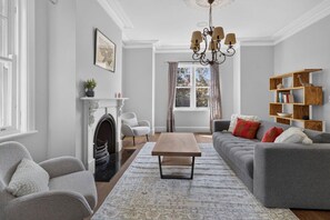 A living room with a fireplace, sofa, armchair, coffee table, and a bookshelf. - Spacious 4-Bed House with Pool in Mosman (Mosman)