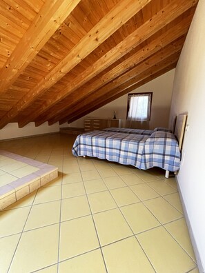 A room with a sloped wooden ceiling, a bed with a checkered bedspread, a dresser, and a window with curtains. - Spacious home with pool and terraces (Provincia di Rovigo)