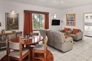 A living room with a round dining table, two sofas, a flat-screen TV, and artwork on the walls.