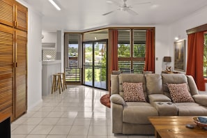 A living room with a sofa, a coffee table, and a ceiling fan. There is a sliding glass door leading to a balcony. - Peaceful 2-Bedroom in Innisfail Cassowary Coast (Belvedere)