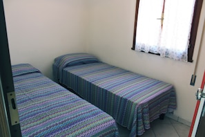 A small room with two single beds, a window with a curtain, and a door. - Comfy home near the beach (Rosolina Mare)