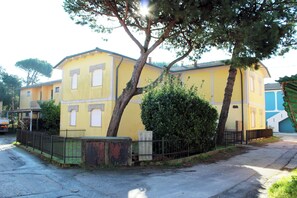 A yellow building with a gated entrance, a small fenced area, and a tree in front. - Comfy home near the beach (Rosolina Mare)
