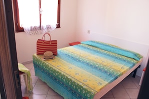 A room with a bed, a small table, a chair, a window with curtains, and a door. - Comfy home near the beach (Rosolina Mare)