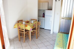 A dining area with a table set for four, a kitchen with a white refrigerator, and a tiled floor. - Comfy home near the beach (Rosolina Mare)