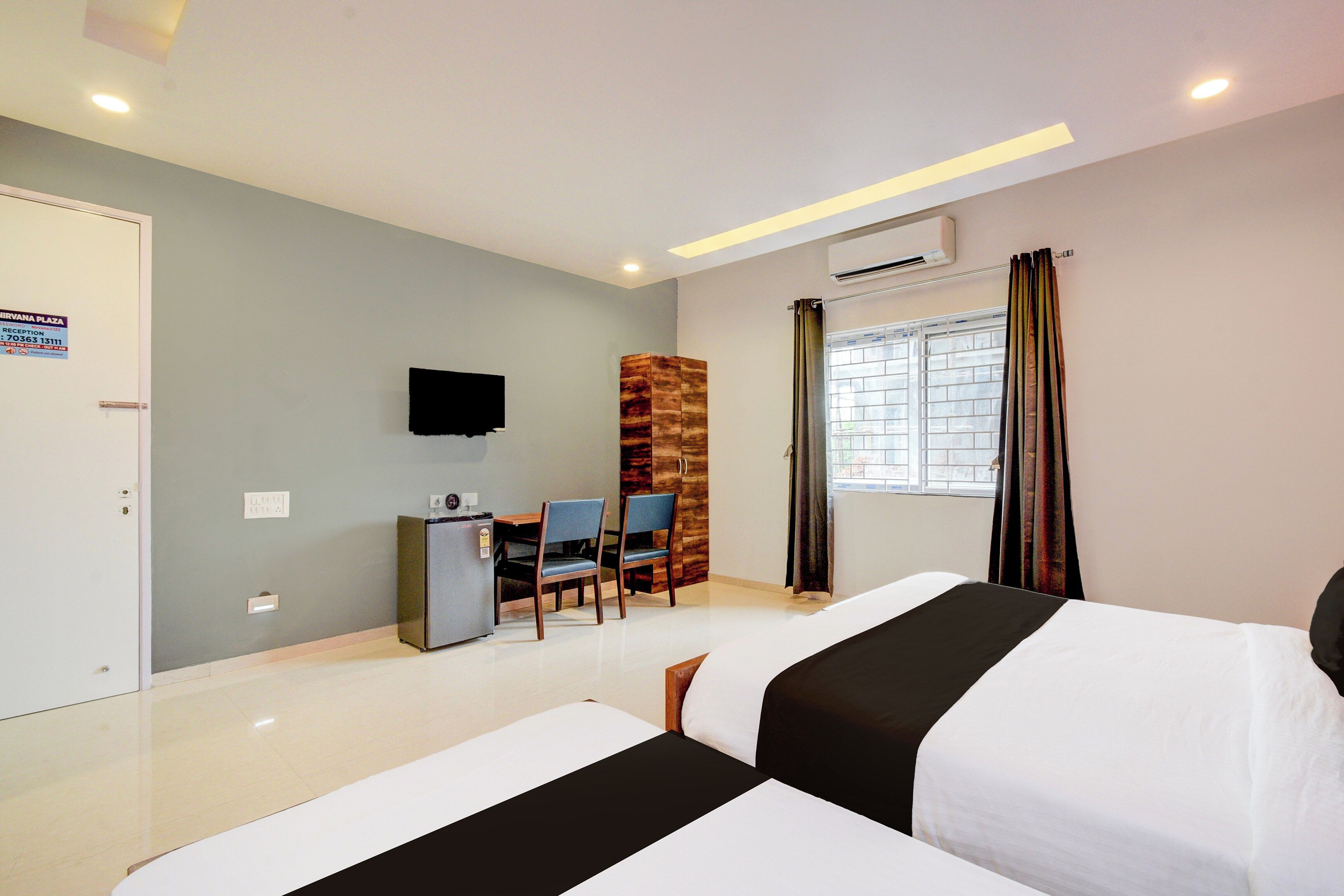 A hotel room with two beds, a desk with chairs, a television, and a window with curtains.