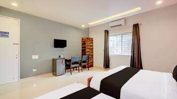 A hotel room with two beds, a desk with chairs, a television, and a window with curtains.