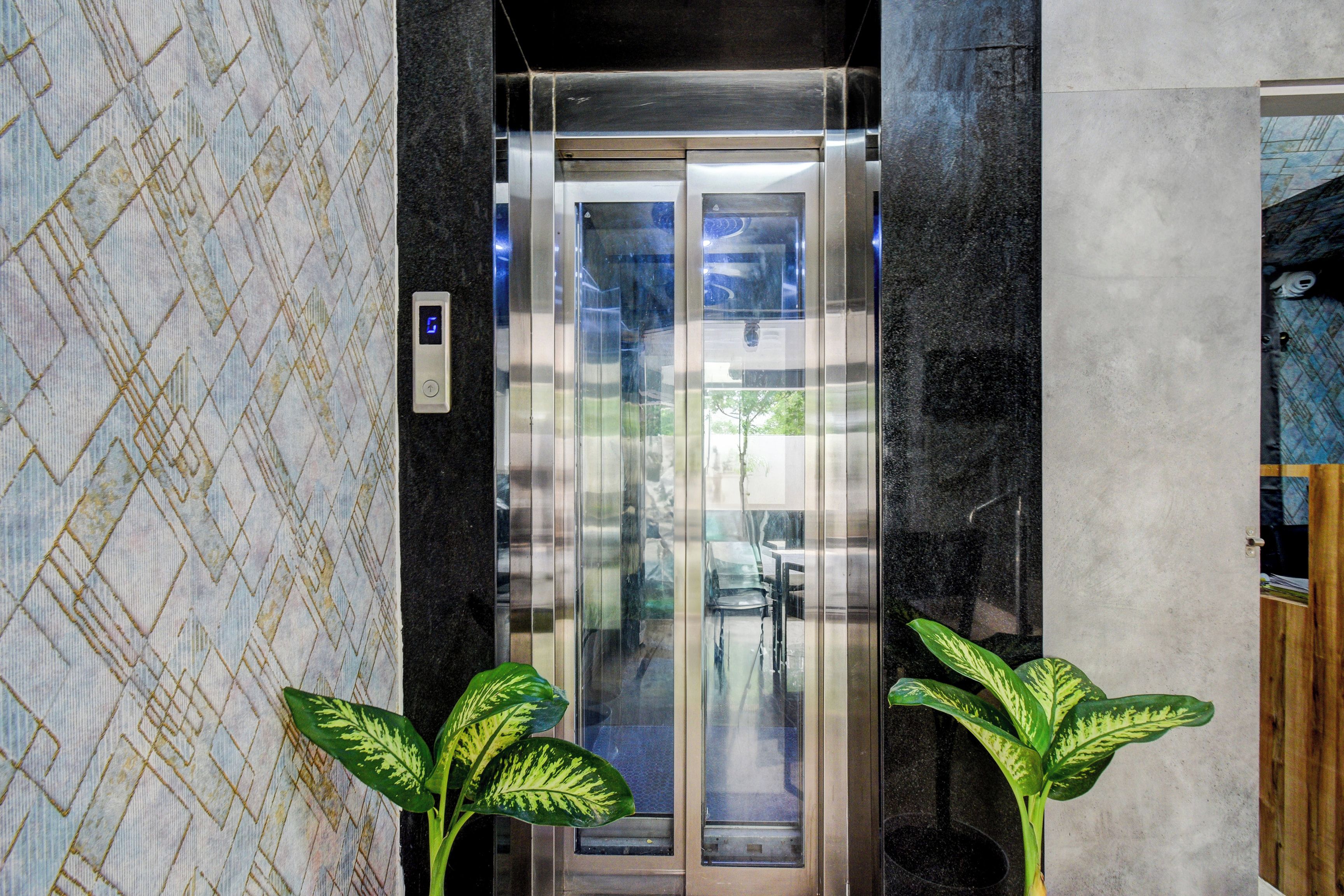 Un ascensor con pantalla digital, puertas de vidrio y un revestimiento de pared con diseño.