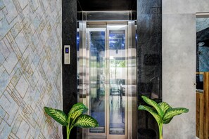 Um elevador com painel digital, portas de vidro e parede estampada.