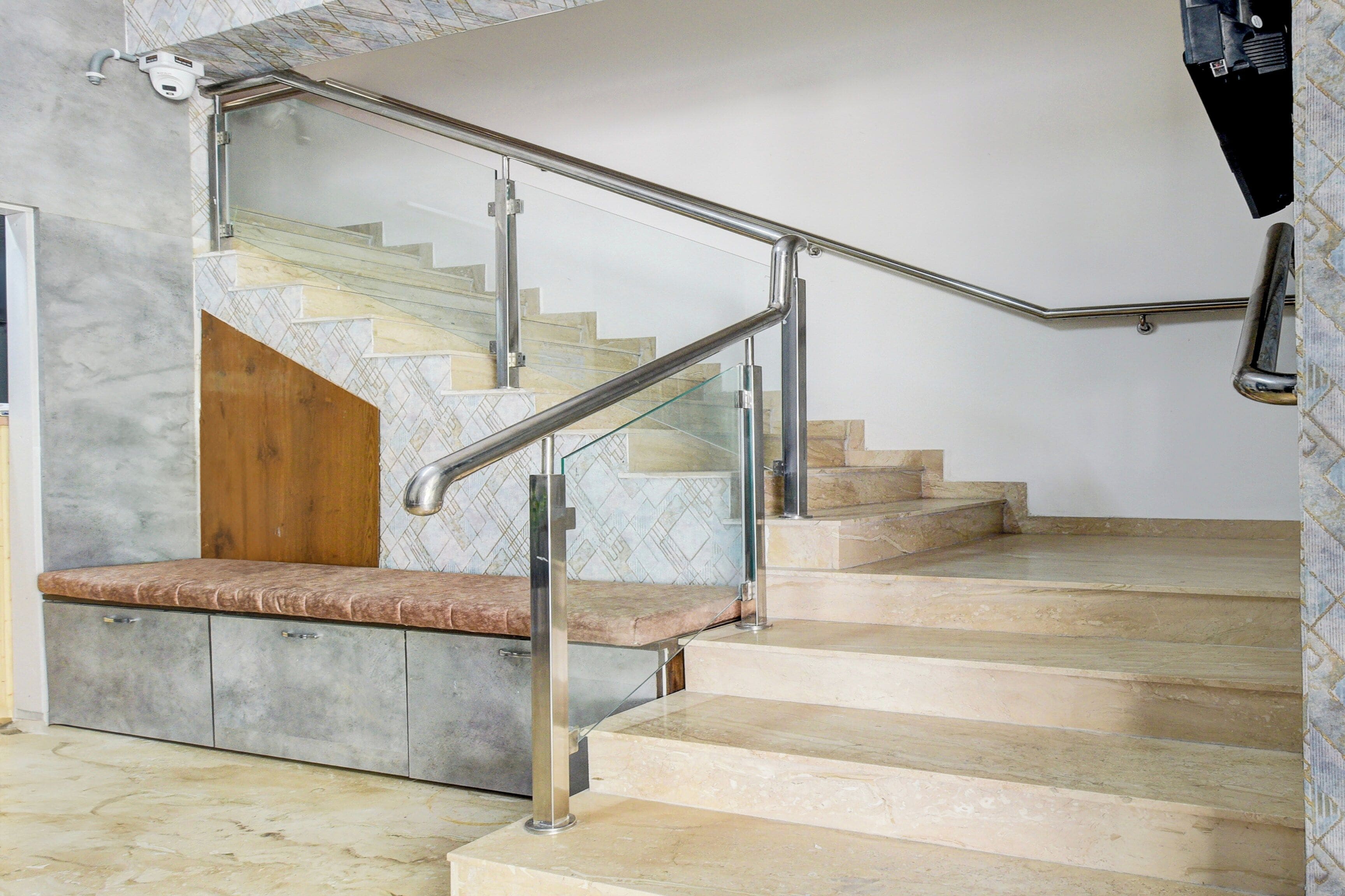Una escalera con barandilla de metal, peldaños de mármol y un banco de madera.
