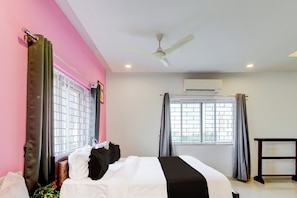Una habitación de hotel con una cama, un ventilador de techo, un equipo de aire acondicionado y ventanas con cortinas.
