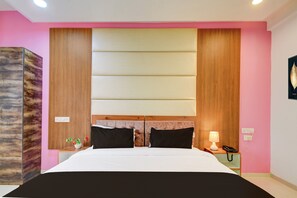 Quarto de hotel com cama, mesas de cabeceira, luminária e telefone fixado na parede.