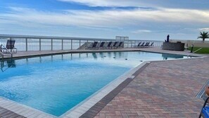 Ein Schwimmbecken mit Meerblick, umgeben von Liegestühlen und einer Pflasterterrasse.