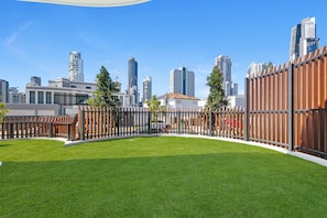 A grassy courtyard with a wooden fence and a city skyline in the background. - Luxury Chevron Island Retreat | Water & City Views (Surfers Paradise)