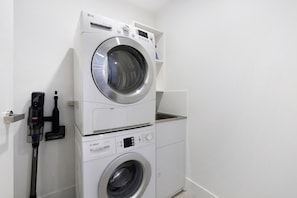 A stacked washer and dryer unit with a Bosch brand label, a control panel, and a hose attached to the wall. - Luxury Chevron Island Retreat | Water & City Views (Surfers Paradise)
