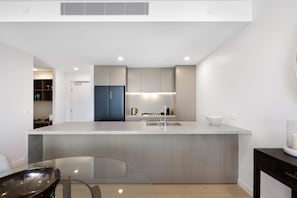 A modern kitchen with a central island, built-in appliances, and a dining area with a glass table. - Luxury Chevron Island Retreat | Water & City Views (Surfers Paradise)