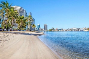A beach with a clear view of a city skyline, palm trees, and a calm sea. - Luxury Chevron Island Retreat | Water & City Views (Surfers Paradise)