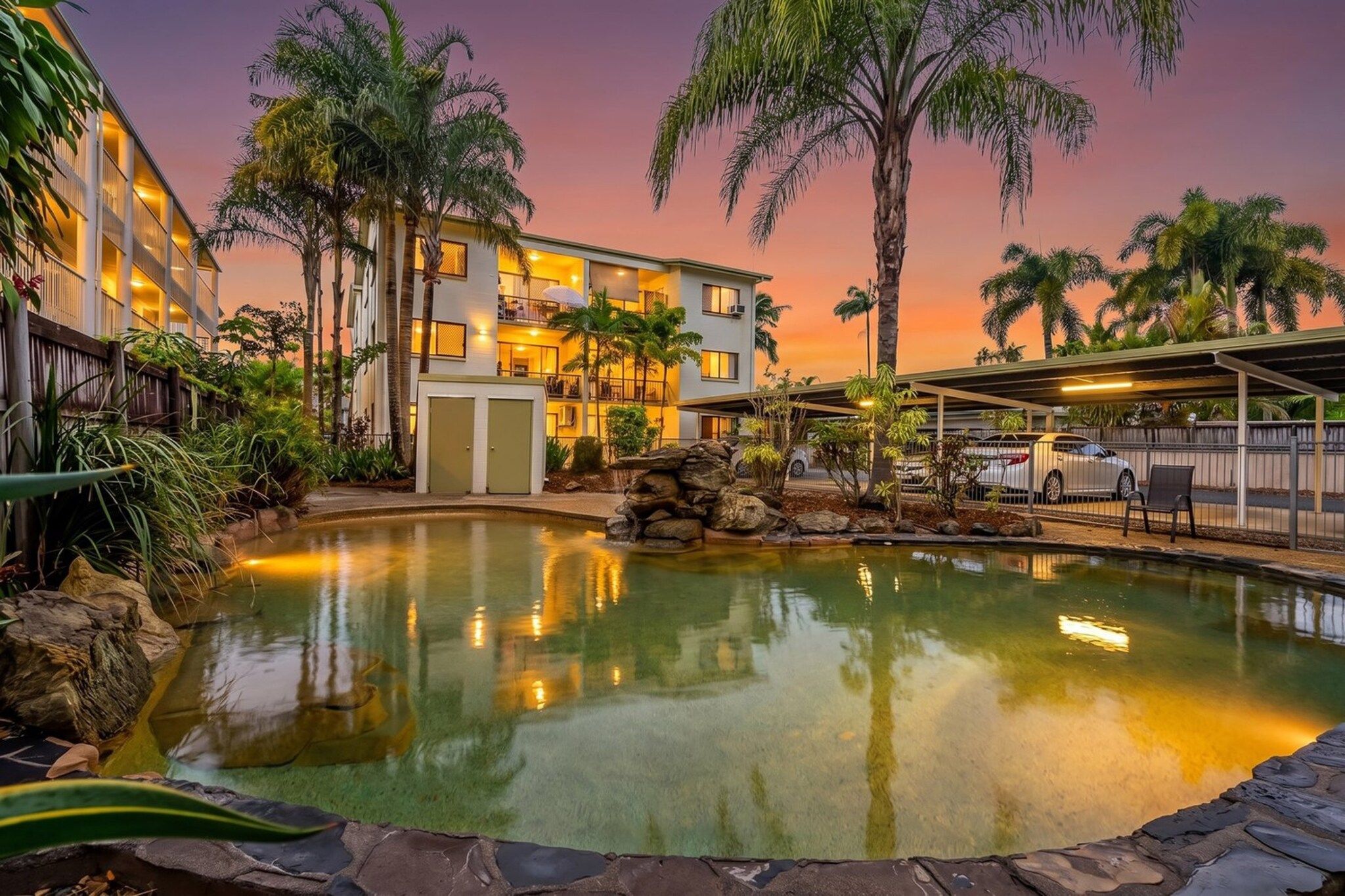 Un hôtel doté d’une piscine, de palmiers et offrant une vue sur un ciel au coucher du soleil.