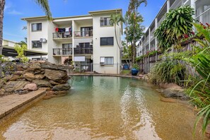 A residential building with a swimming pool, surrounded by tropical plants and a rocky landscape. - Bright 2-Bed Apartment Near Cairns Esplanade (Cairns North)