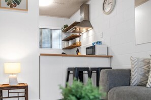 A modern kitchen with white cabinets, a microwave, and a stove. There are wooden shelves above the counter and a clock on the wall. - Bright 2-Bed Apartment Near Cairns Esplanade (Cairns North)