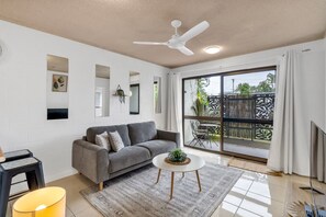 Ein modernes Wohnzimmer mit einem grauen Sofa, einem runden Couchtisch und einem Deckenventilator.