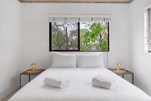 A hotel room with a large bed, two bedside tables, and a window with a view of trees. - Bright 2-Bed Apartment Near Cairns Esplanade (Cairns North)