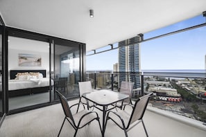 Ein Balkon mit einem Bett, einem Tisch und Stühlen mit Blick auf eine Stadtlandschaft und das Meer.