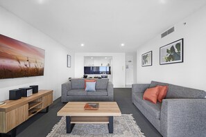 A modern living room with a grey sofa, a coffee table, and a TV on a wooden stand. - Ocean View | Circle on Cavill 2BR Apartment (Surfers Paradise)