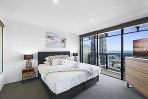 Ein modernes Schlafzimmer mit einem großen Bett, einem Nachttisch, einer Kommode und Blick auf die Stadt durch raumhohe Fenster.