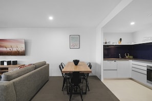 A modern living room with a sofa, a dining table, and a kitchen area with appliances. - Ocean View | Circle on Cavill 2BR Apartment (Surfers Paradise)