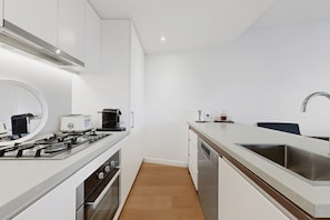 A modern kitchen with white cabinetry, a stainless steel sink, a built-in oven, and a gas stove. - High-Rise 1-Bed Apartment Near Brisbane CBD (Fortitude Valley)