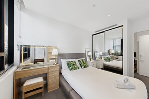 A modern hotel room with a large bed, a wooden desk with drawers, a mirror, and a bedside table with lamps. - High-Rise 1-Bed Apartment Near Brisbane CBD (Fortitude Valley)