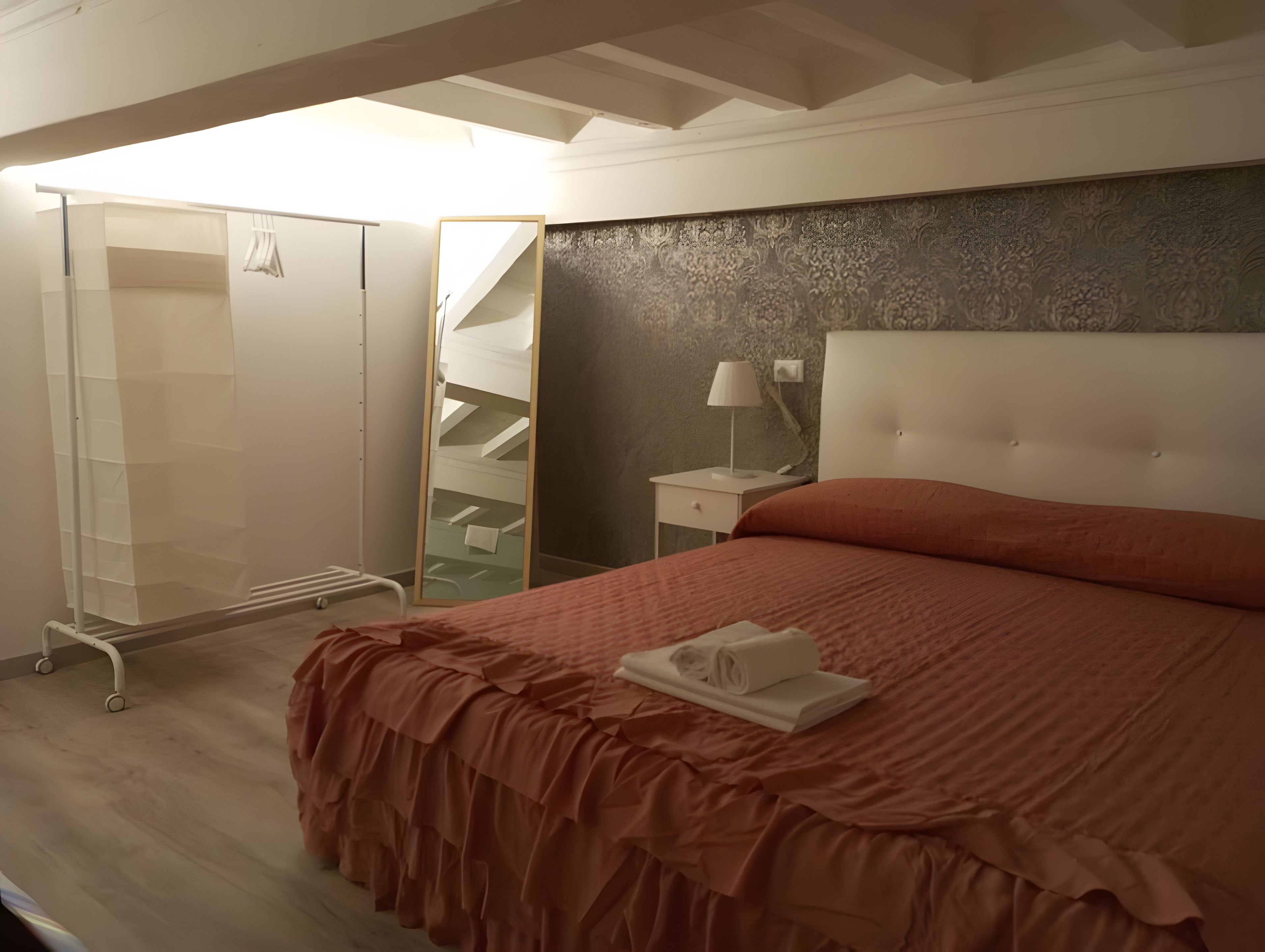 Une chambre à coucher comprenant un lit, une table de chevet, un miroir, une armoire et un escalier.