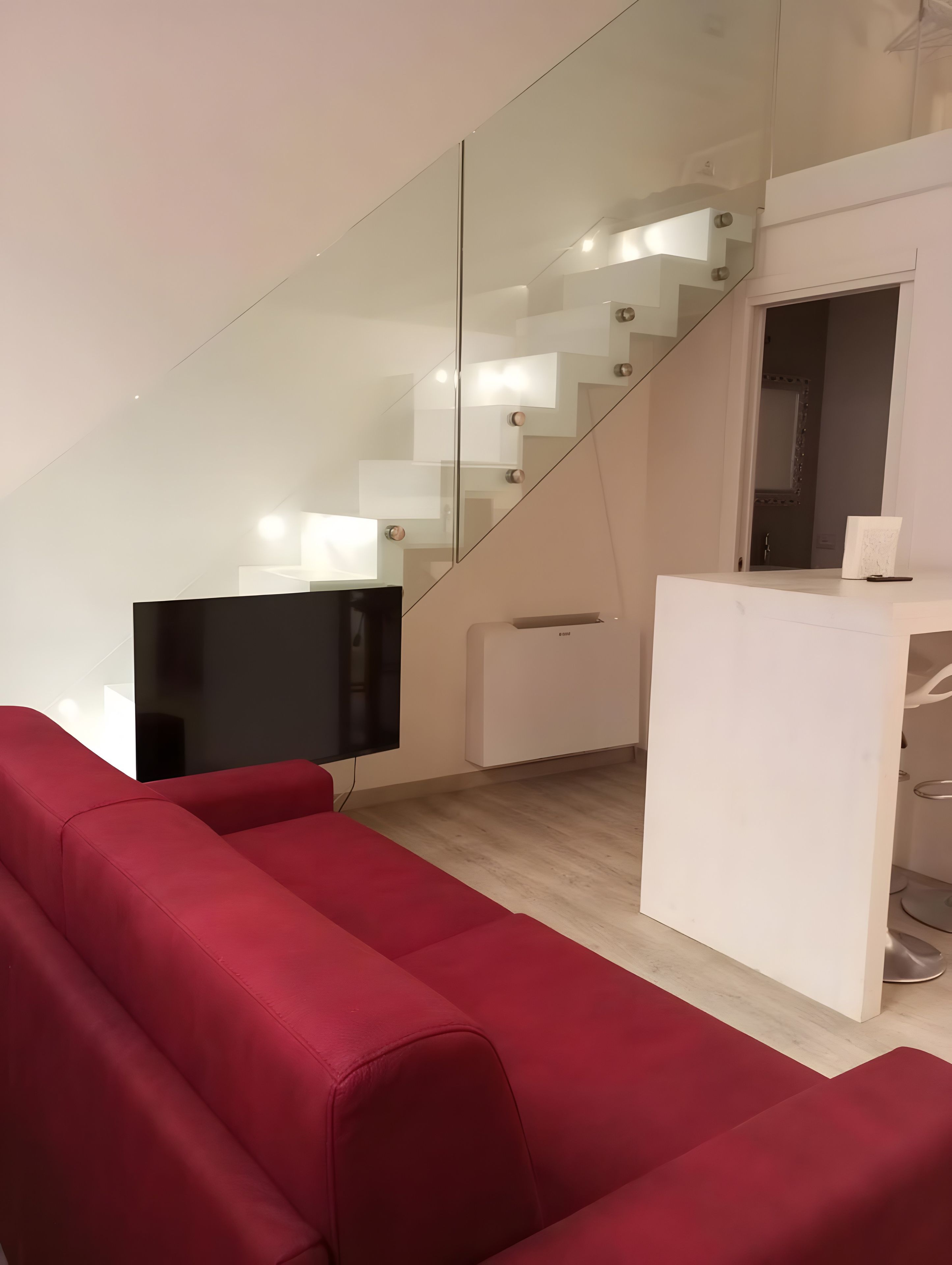 Un intérieur moderne avec un canapé rouge, un téléviseur à écran plat, un bureau blanc et un escalier en verre.