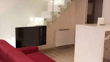 Un intérieur moderne avec un canapé rouge, un téléviseur à écran plat, un bureau blanc et un escalier en verre.