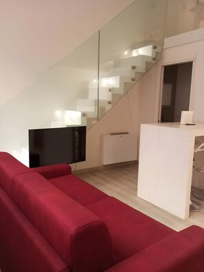 Ein modernes Interieur mit einem roten Sofa, einem Flachbildfernseher, einem weißen Schreibtisch und einer Glastreppe.