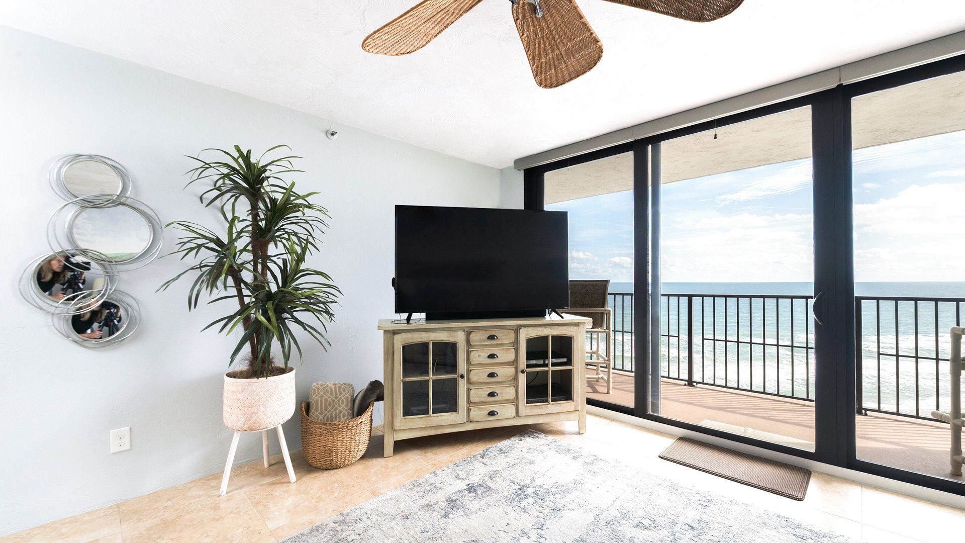 A balcony with a view of the ocean, a television on a cabinet, and a potted plant.