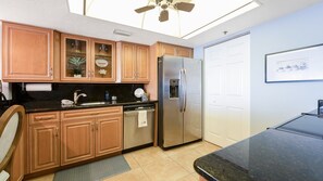 A kitchen with wooden cabinets, a stainless steel refrigerator, a dishwasher, and a ceiling fan. - #806 Ashley 2/2 Oceanfront Condo Daytona Beach Shores (Daytona Beach Shores)