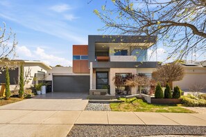 A modern two-story house with a flat roof, a visible garage, and a landscaped front yard with various plants. - 4-Bed Retreat With Cinema in Wright (Wright)
