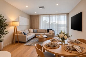 A modern living room with a sofa, coffee table, dining table set for four, and a large window with curtains. - Spacious 3-Bed Townhouse In Mile End (Mile End)