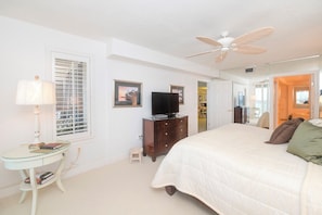 Quarto com cama, televisão, cômoda, luminária e ventilador de teto.