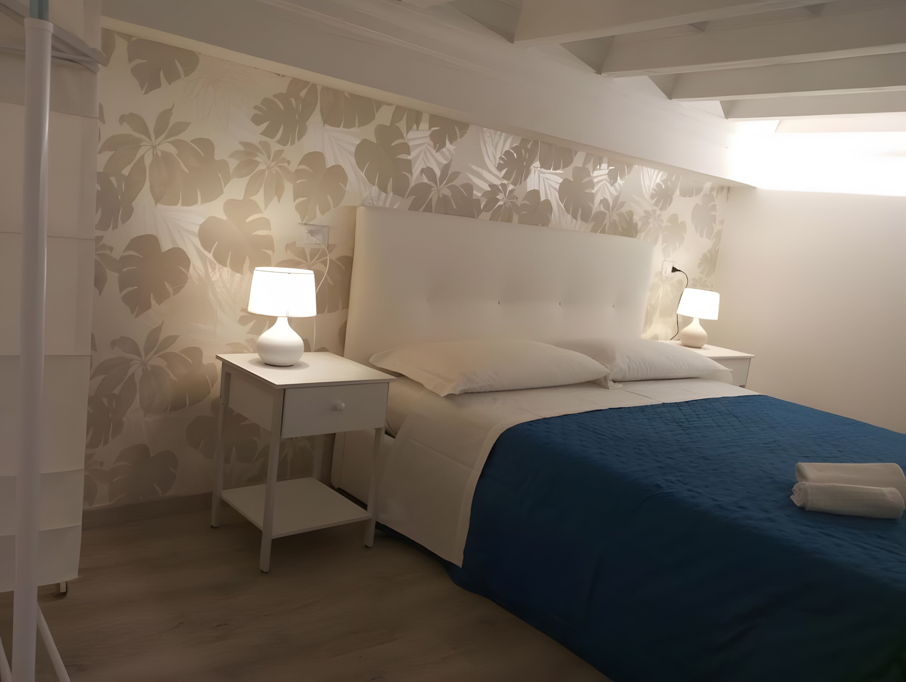 Una camera da letto con un letto, due comodini con lampade, un tavolino da notte e carta da parati floreale.